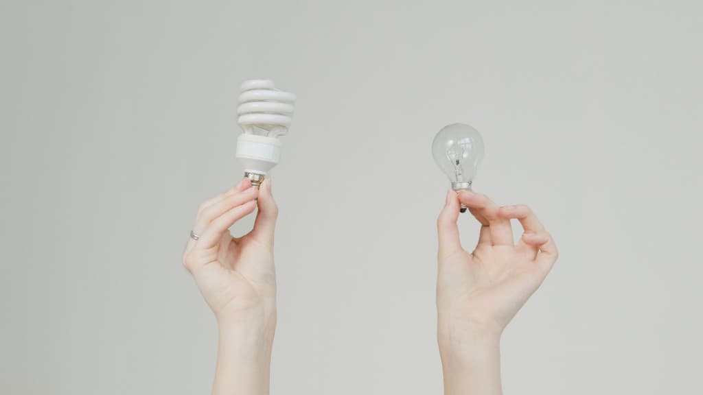 Zwei Hände halten eine Energiesparlampe und eine Glühlampe nebeneinander