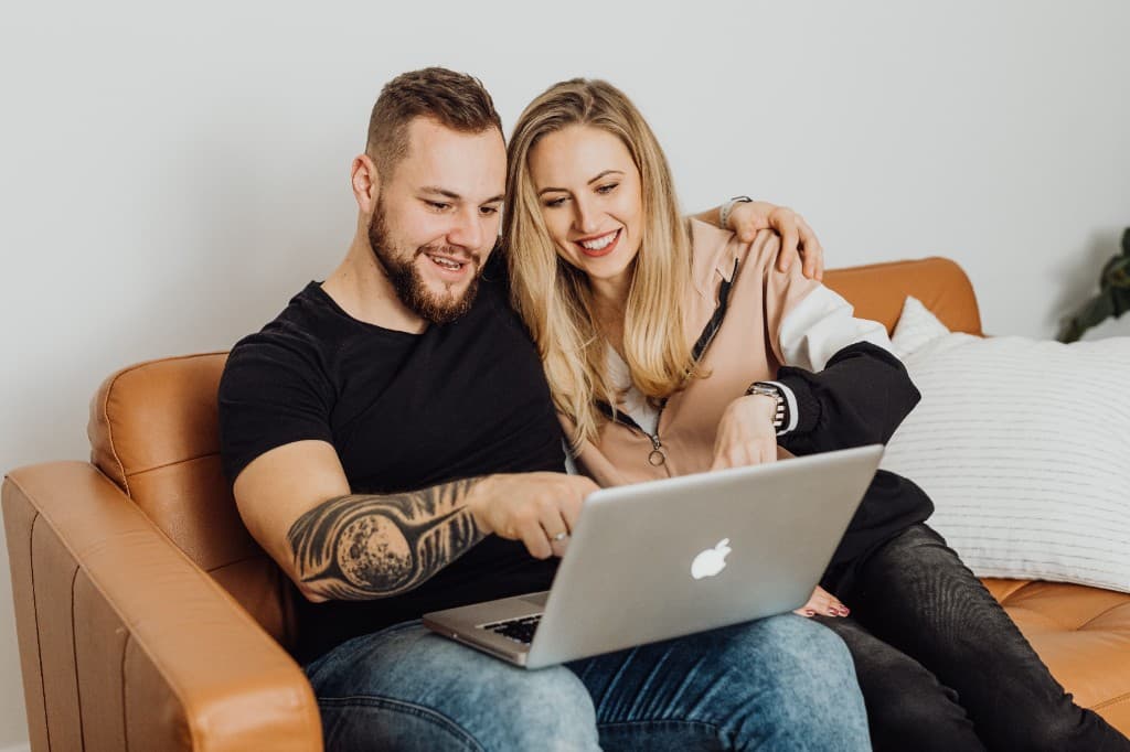 Ein Paar sitzt auf einem Sofa und sieht gemeinsam auf einen Laptop